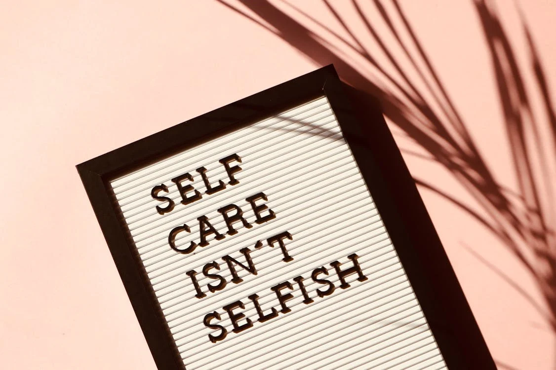 A letterboard sign with the message "SELF CARE ISN'T SELFISH" against a pink background with plant shadows. A letterboard sign with the message "SELF CARE ISN'T SELFISH" against a pink background with plant shadows.