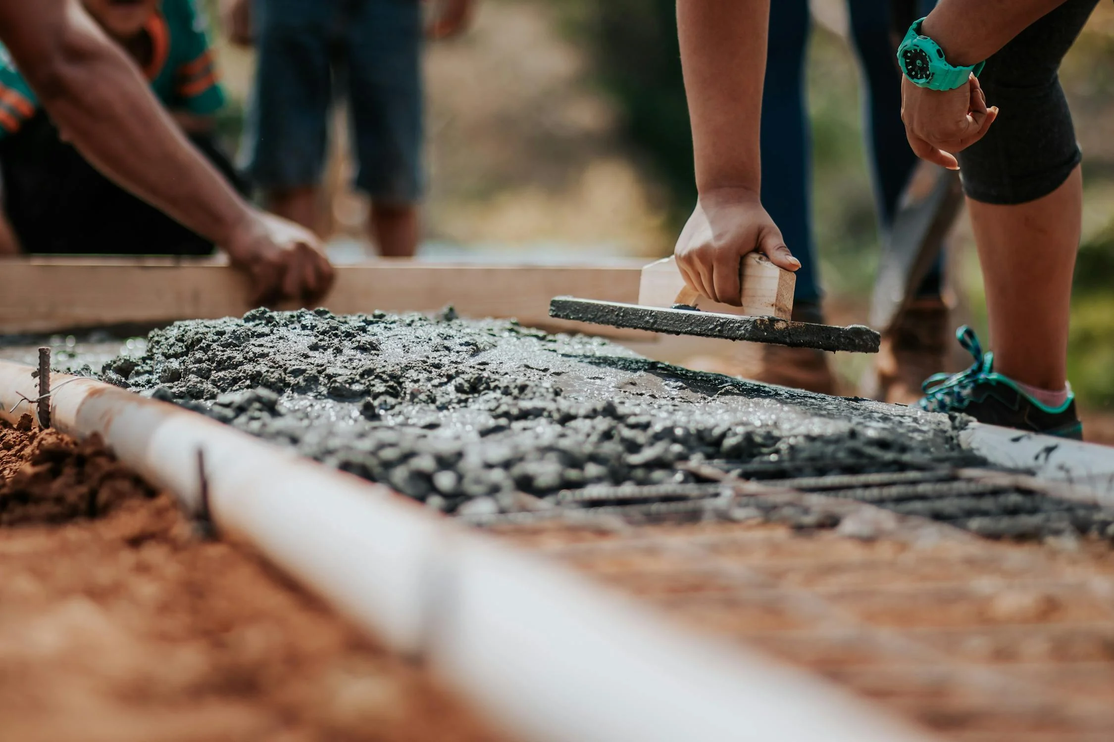 Close-up of hands smoothing wet concrete with tools, showing people working together on a construction project outdoors with one person wearing a turquoise watch. Close-up of hands smoothing wet concrete with tools, showing people working together on a construction project outdoors with one person wearing a turquoise watch.